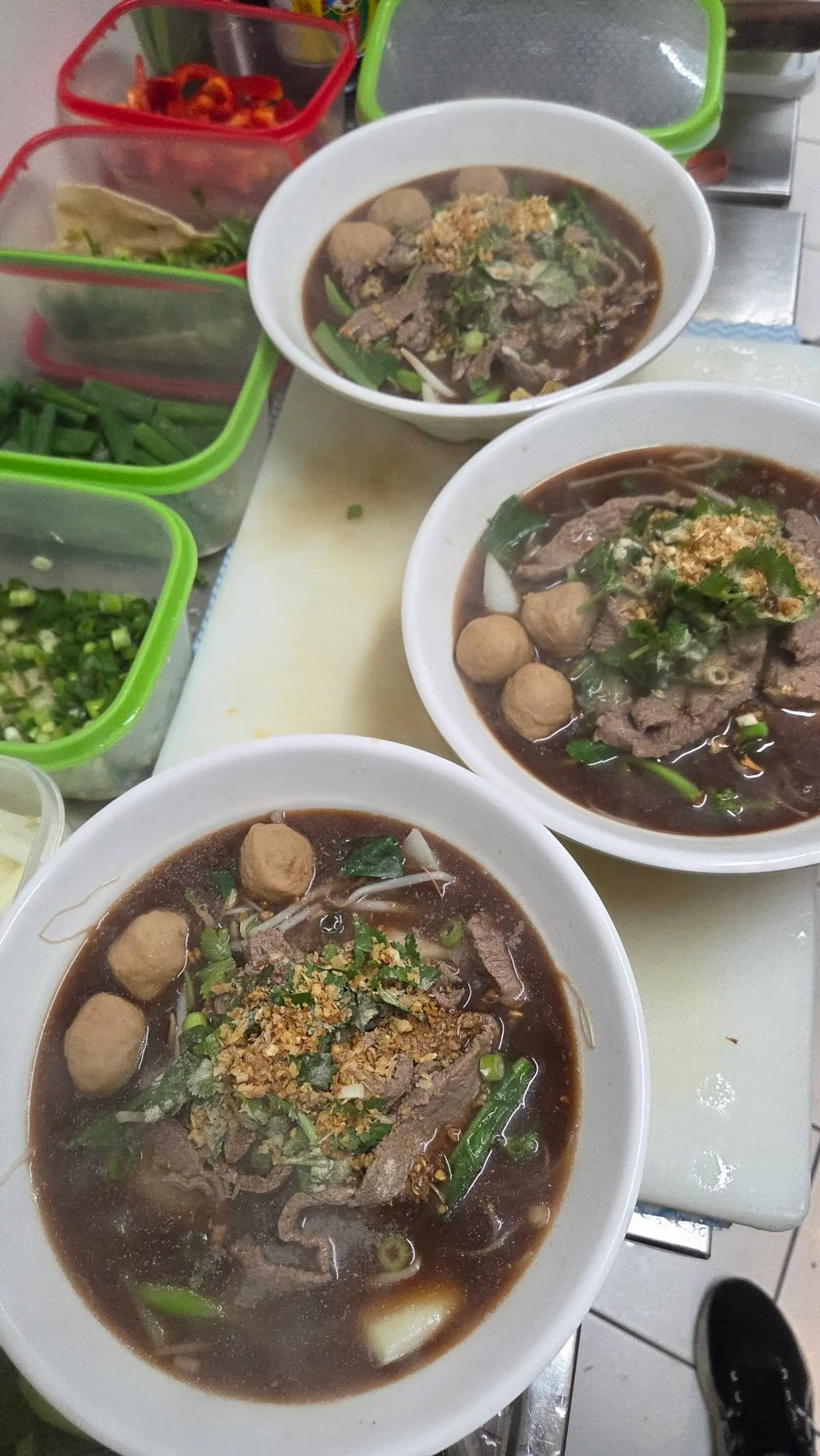Three bowls of dark beef noodle soup with meatballs and spring onions